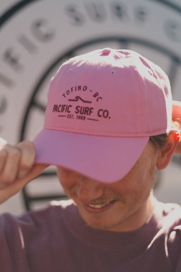 Person wearing a pink cap with 'Tofino BC Pacific Surf Co.' text, blurred background